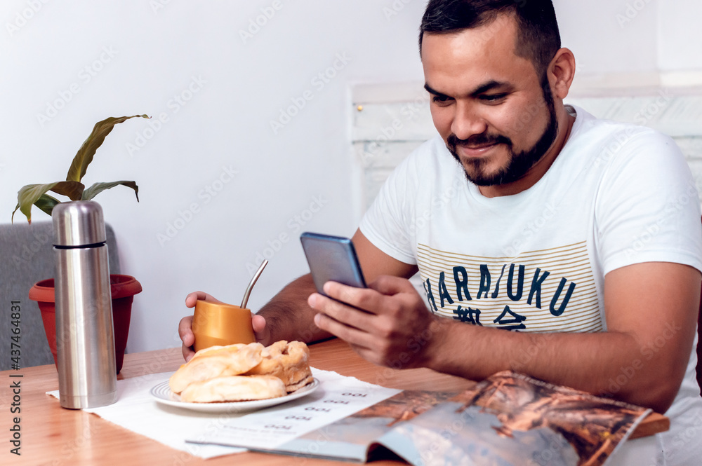 boy who is checking his cell phone while eating sweets for breakfast and drinking mate. boy who is checking his cell phone while eating sweets for breakfast and drinking mate.