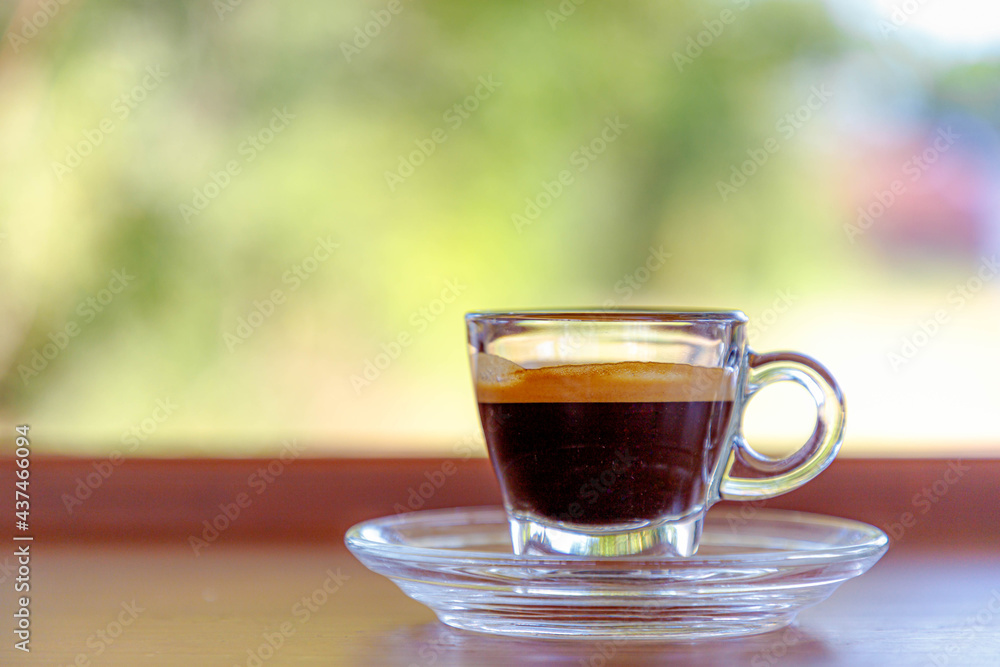 Selective focus of small cup of espresso in glassware on the wooden table, Outdoor drinking coffee in the garden with blurred green background.
