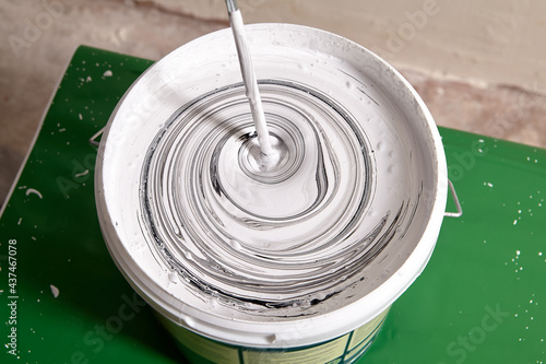 Canvas Print Adding black pigment to white wall paint for mixing in bucket using an electric mixer until gray color is obtained
