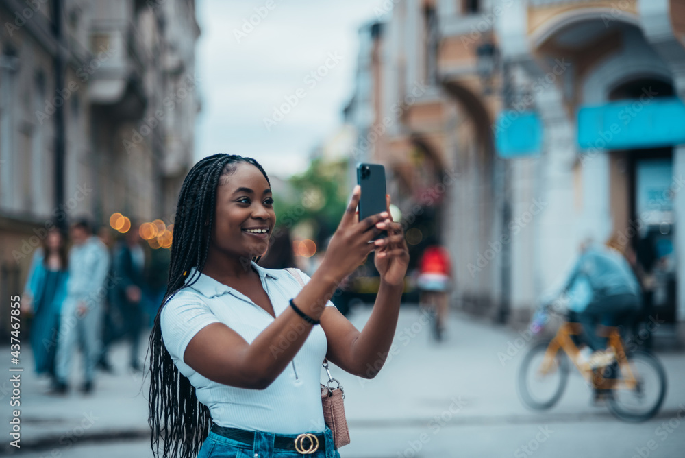 Cheerful african american woman taking selfie with her smartphone while outside in the city