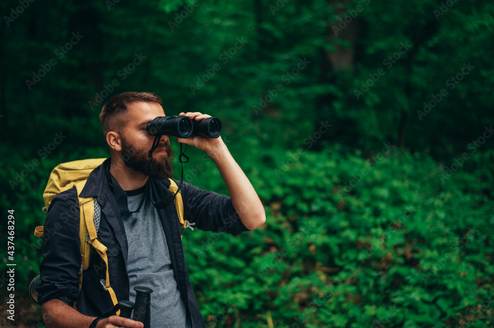 A hiker man walking in the forest using trekking poles and binoculars