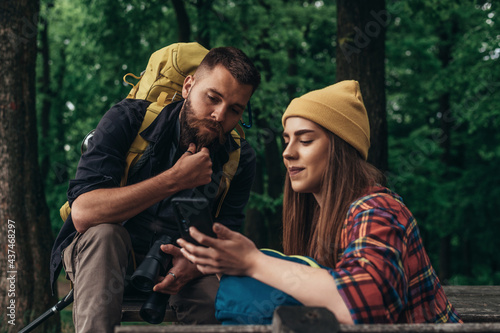 Hikers sitting on a bench in the forest and making a break while using a smartphone