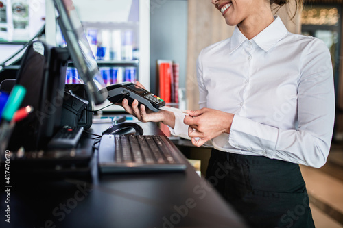 Female bartender holding a credit card reader machine and a payment card to charge the customer bill.