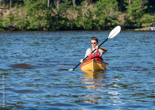 Young man in lifejacket paddling a pack canoe using a kayak paddle on a lake in West Virginia