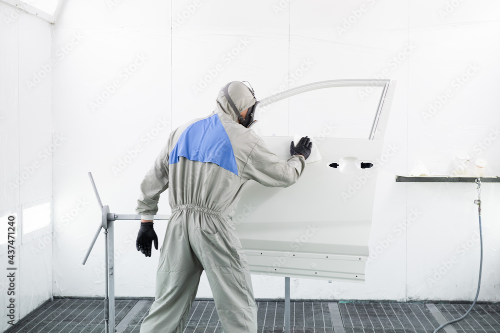 a worker in a gray protective suit are cleaning car door parts.  hard work. mask and protective shield.