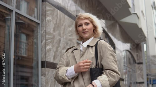 Wallpaper Mural Young blonde woman in a beige trench coat and white blouse stands on the background of a modern office building Torontodigital.ca