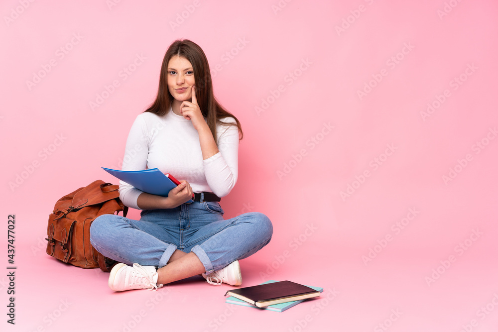 Teenager caucasian student girl sitting on the floor isolated on pink background Looking front Teenager caucasian student girl sitting on the floor isolated on pink background Looking front