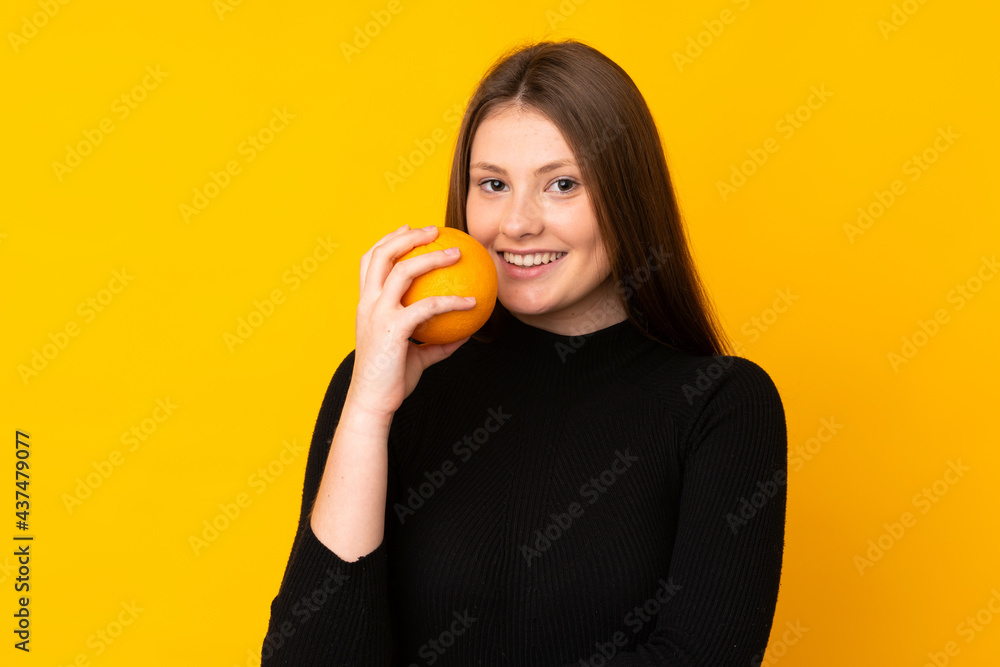 Teenager caucasian girl holding an orange over isolated yellow background Teenager caucasian girl holding an orange over isolated yellow background