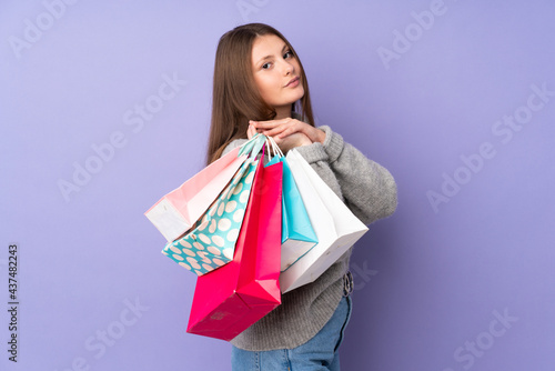 Teenager caucasian girl isolated on purple background holding shopping bags