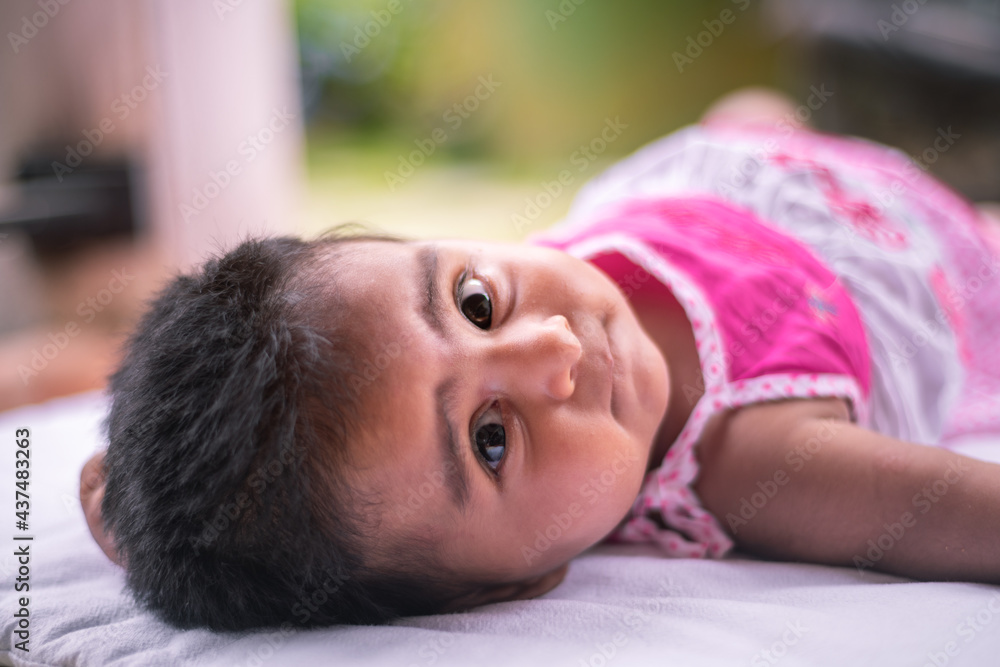 Cute little baby girl lying on a mat and looking behind her, the little princess, jewel of the mother's world. Adorable in a pink dress. Cute little baby girl lying on a mat and looking behind her, the little princess, jewel of the mother's world. Adorable in a pink dress.