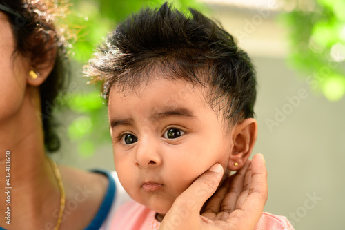 Ear piercing day photoshoot of a cute 4 months old baby girl. small gold earring in her ears. Kids face close-up as her mother holds the baby's ear.