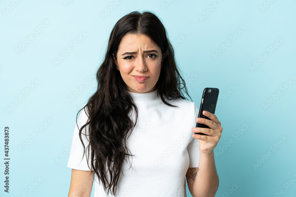 Young woman using mobile phone isolated on blue background with sad expression Young woman using mobile phone isolated on blue background with sad expression