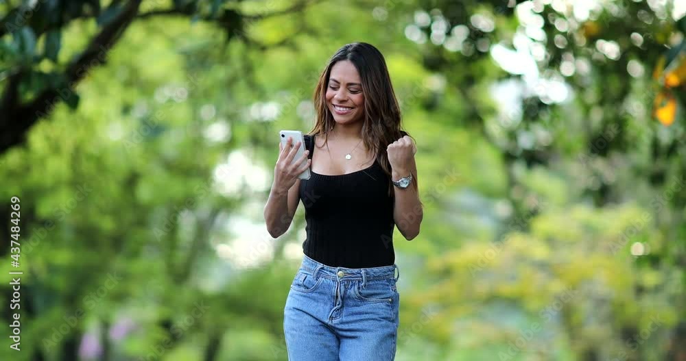 Hispanic woman celebrating good news message on cellphone device outside Hispanic woman celebrating good news message on cellphone device outside