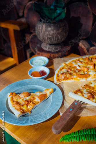 Homemade pizza on brown paper on wooden table with green leaf and white cream