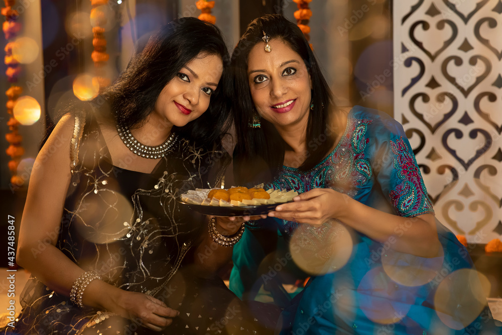 Portrait of two Indian woman sharing sweets on the festive occasion of Diwali. Celebrations at home.