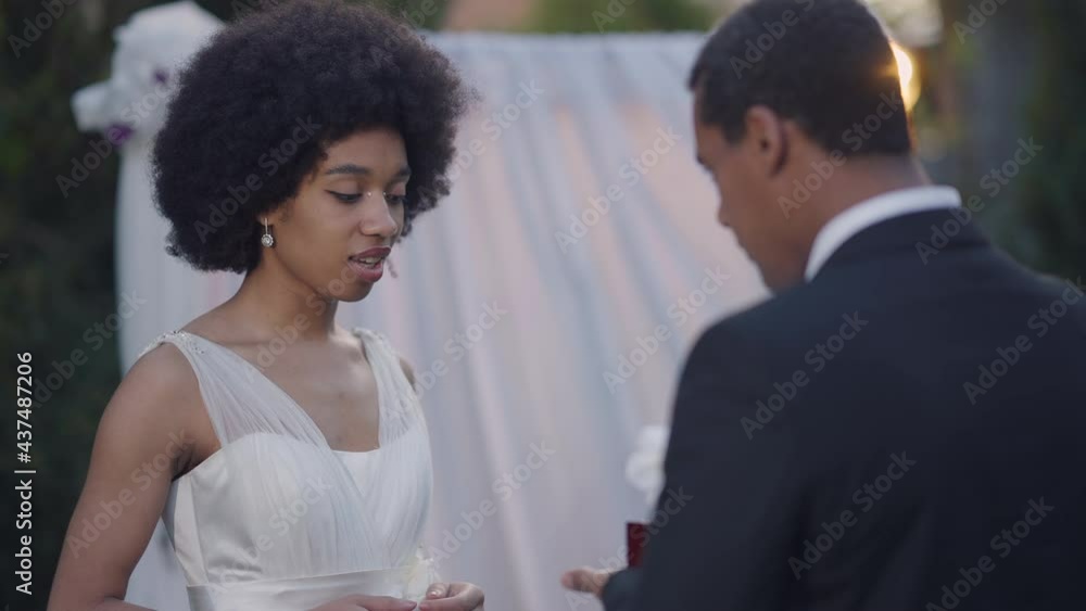 Portrait of young African American woman with excited facial expression looking at wedding rings as man proposing again on marriage ceremony. Happy bride in white dress outdoors Portrait of young African American woman with excited facial expression looking at wedding rings as man proposing again on marriage ceremony. Happy bride in white dress outdoors