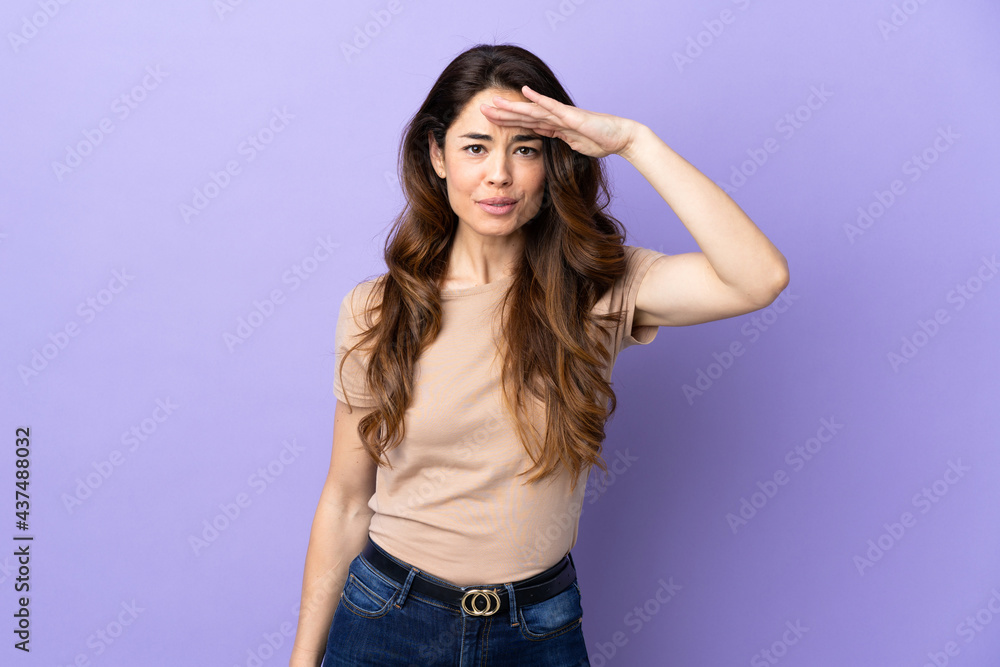 Woman over isolated purple background looking far away with hand to look something Woman over isolated purple background looking far away with hand to look something