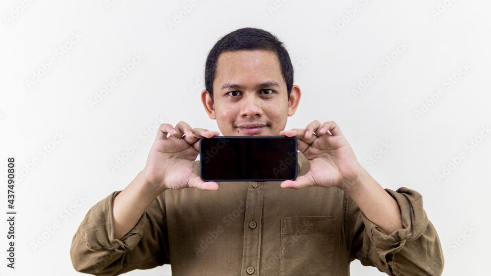 Smiling face expression of young Asian Malay man holding smartphone with empty black screen. Smiling face expression of young Asian Malay man holding smartphone with empty black screen.