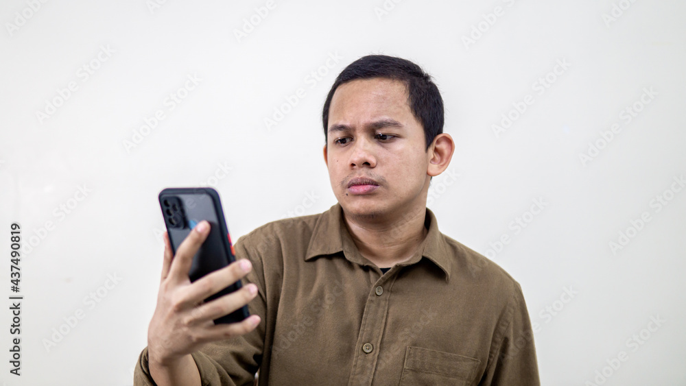 Serious and thoughtful face expression of young Asian Malay man looking at the smartphone. Serious and thoughtful face expression of young Asian Malay man looking at the smartphone.
