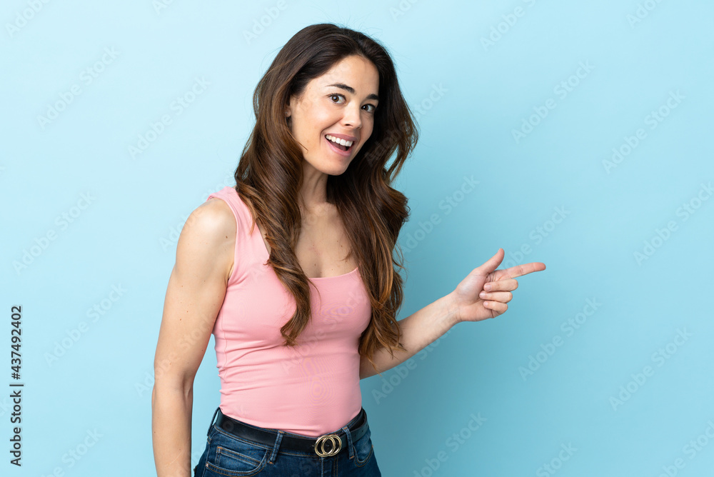Woman over isolated blue background surprised and pointing finger to the side Woman over isolated blue background surprised and pointing finger to the side