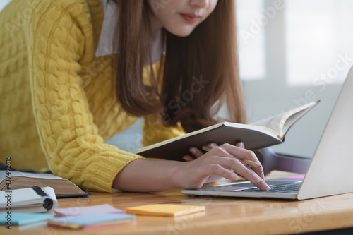 Student studying and writing notes in a notebook at home, making research on laptop and browse internet, watching online webinar, listening audio course, e-learning education concept