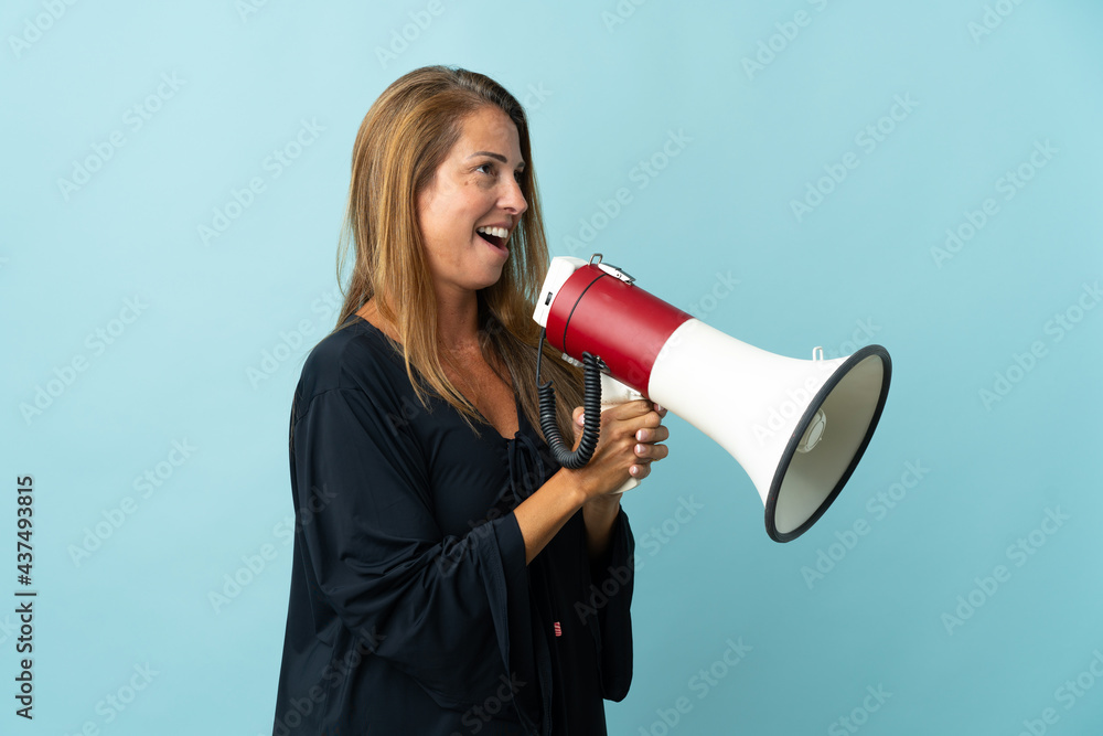 Middle age brazilian woman isolated on blue background shouting through a megaphone Middle age brazilian woman isolated on blue background shouting through a megaphone