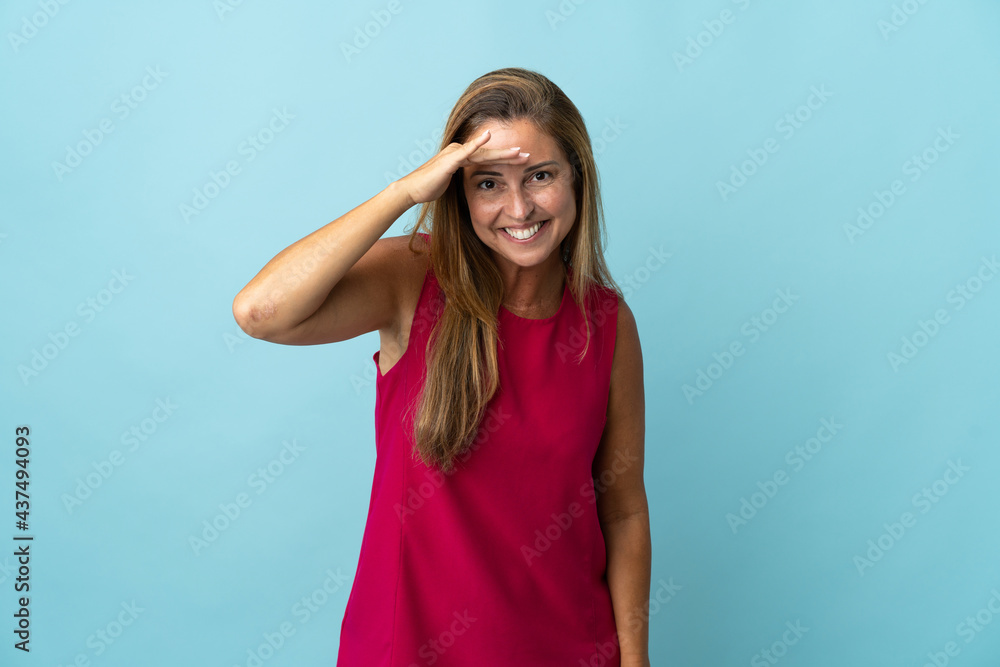 Middle age brazilian woman isolated on blue background looking far away with hand to look something