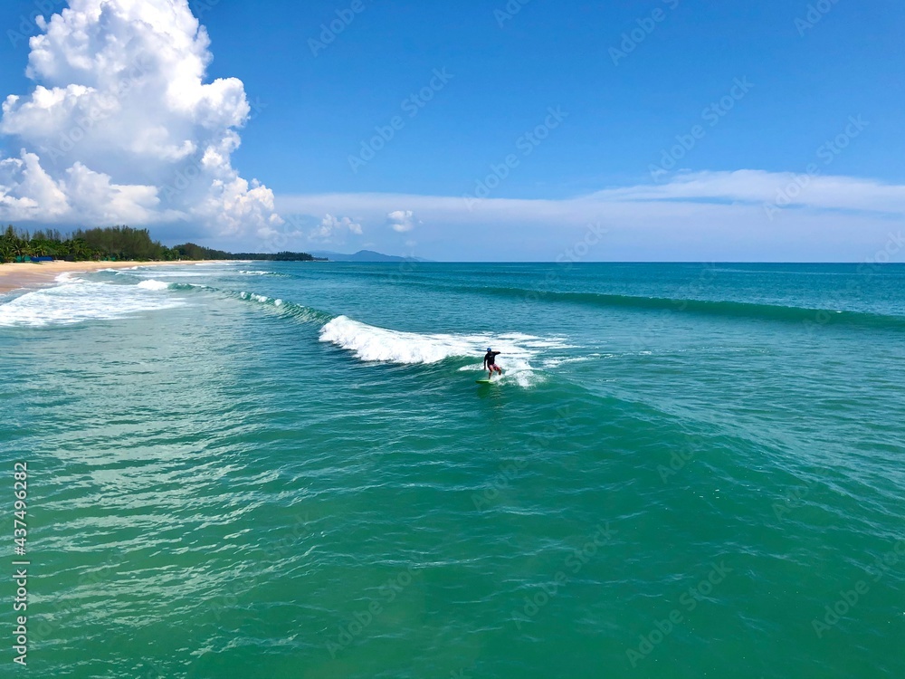 Fototapeta premium A young man surfer riding waves at Natai beach in Phang Nga, Thailand. Asian man catching waves in blue ocean. Surfing action water board sport.