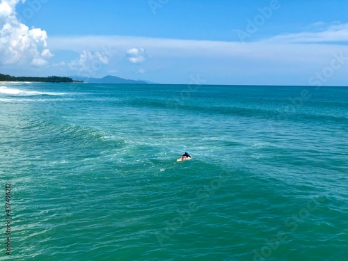 A young man surfer riding waves at Natai beach in Phang Nga, Thailand. Asian man catching waves in blue ocean. Surfing action water board sport.