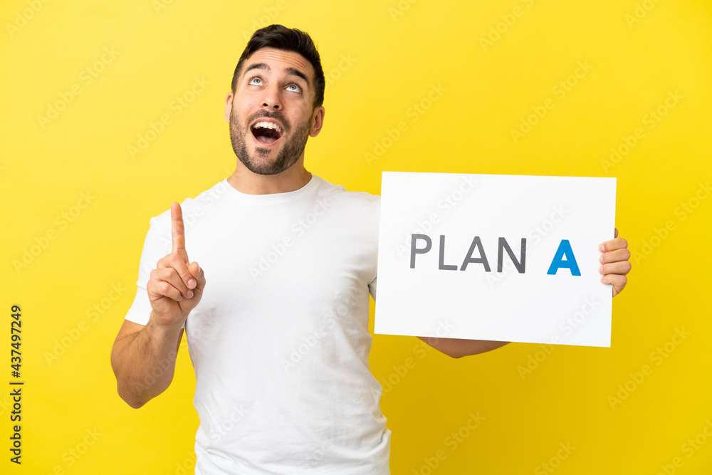 Young handsome caucasian man isolated on yellow background holding a placard with the message PLAN A and thinking Young handsome caucasian man isolated on yellow background holding a placard with the message PLAN A and thinking