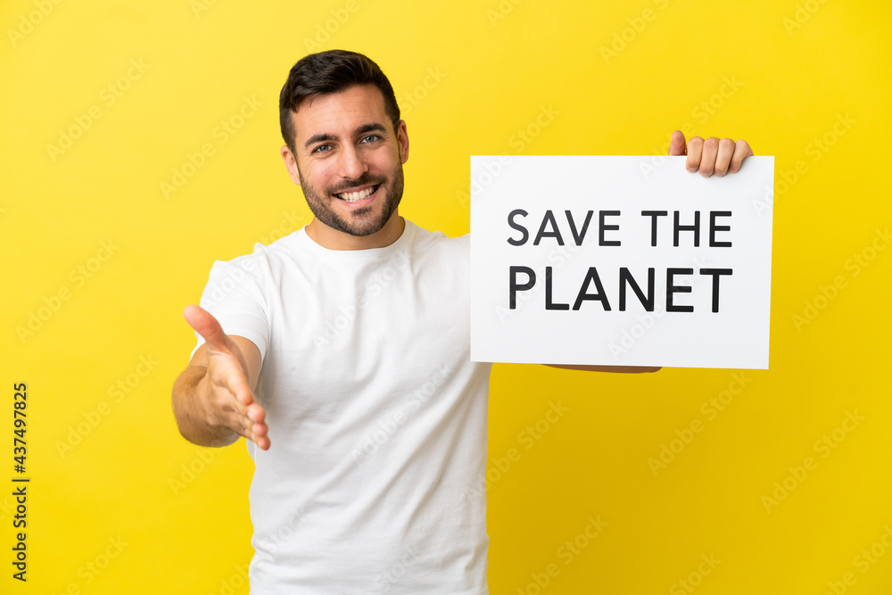 Young handsome caucasian man isolated on yellow background holding a placard with text Save the Planet making a deal Young handsome caucasian man isolated on yellow background holding a placard with text Save the Planet making a deal