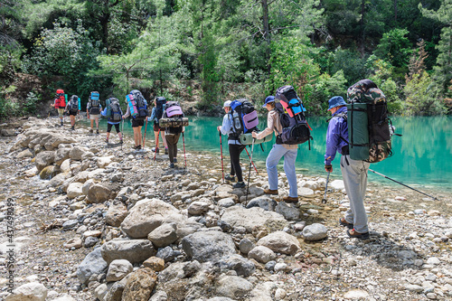 A group of tourists with large backpacks cross the river over the rocks in the goynuk canyon on the Lycian trail in Turkey