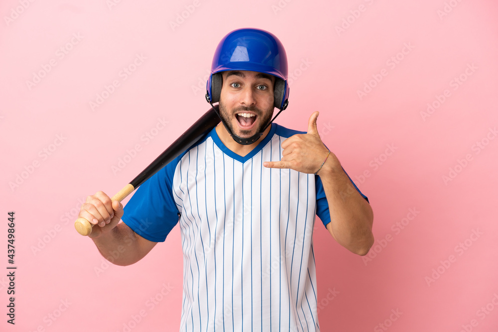 Baseball player with helmet and bat isolated on pink background making phone gesture. Call me back sign