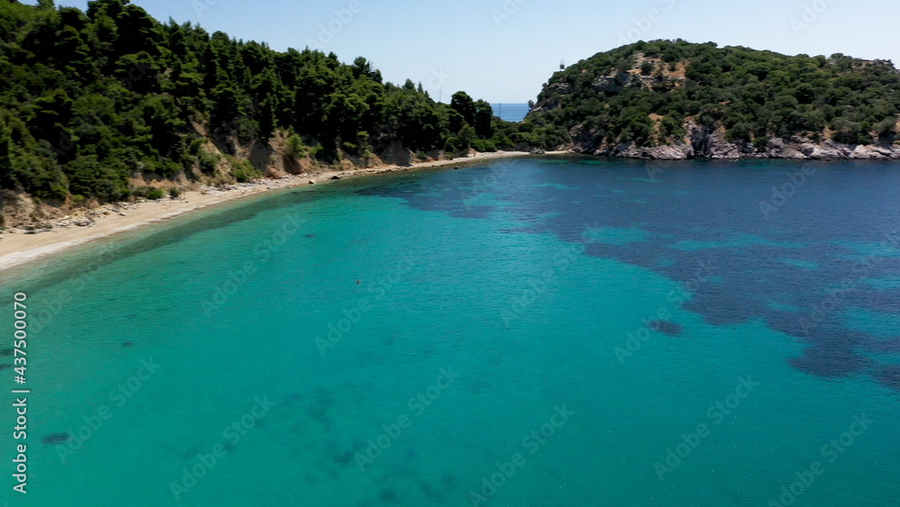 Aerial drone views over a rocky coastline, crystal clear Aegean sea waters, touristic beaches and lots of greenery in Skopelos island, Greece. A typical view of many similar Greek islands.