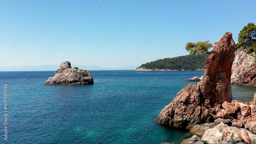 Fototapeta premium Aerial drone views over a rocky coastline, crystal clear Aegean sea waters, touristic beaches and lots of greenery in Skopelos island, Greece. A typical view of many similar Greek islands.