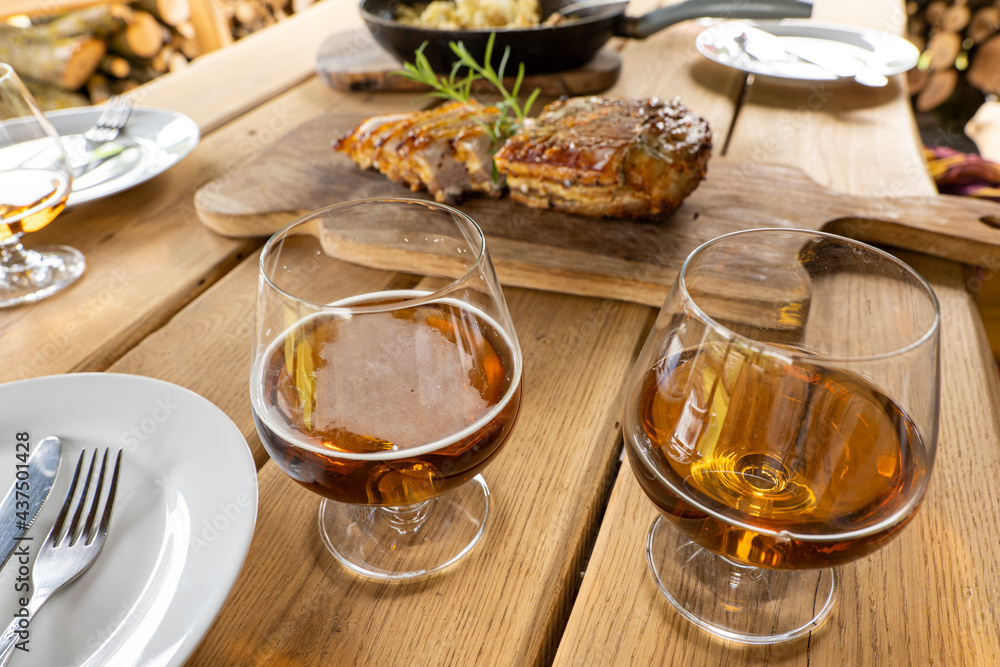 Meal, party in the foreground glasses with beer, brandy, in the background baked bacon lies on a wooden board, decorated with herbs Meal, party in the foreground glasses with beer, brandy, in the background baked bacon lies on a wooden board, decorated with herbs