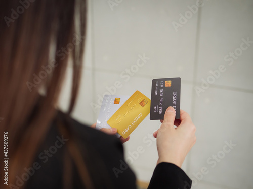 Close-up of three mockup credit cards in a businesswoman's hands, a rear view of a businesswoman in a black suit is holding three mockup credit cards in her hands.
