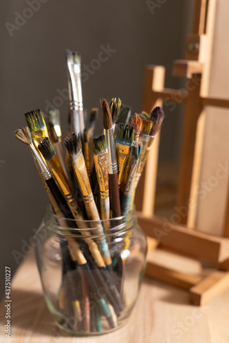 Paint brush in glass jar on wooden table background texture. Paintbrush and easel as painter abstract art concept