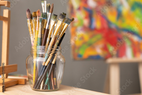 Paint brush in glass jar on wooden table background. Paintbrush and painting as art concept