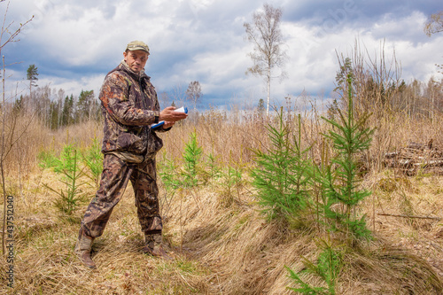 A forest engineer stands in the forest next to young spruce trees.