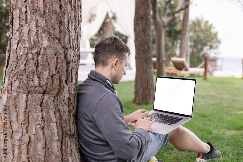 A young man with laptop with blank white screen outdoor. Freelance work from anywhere in the world A young man with laptop with blank white screen outdoor. Freelance work from anywhere in the world