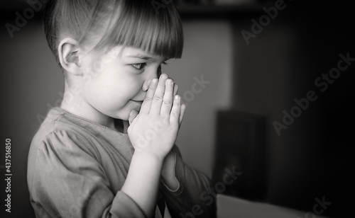 Pretty baby girl praying at home monochrome banner photo. A black-and-white photo of a girl who folded her hands in prayer and supplication. Faith, hope, love. The concept of religion.