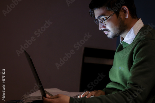 A young handsome indian boy working on laptop.