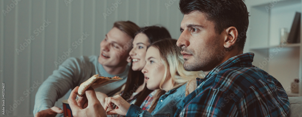 The four people with a pizza watch a movie on the sofa