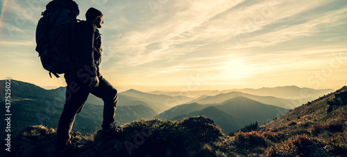 The man standing with a camping backpack on a rock with a picturesque sunset © realstock1