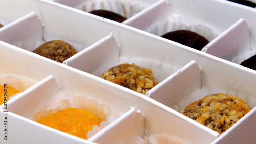 Different coloured natural candies lie in white designed paper box under electric light at confectionery super closeup Different coloured natural candies lie in white designed paper box under electric light at confectionery super closeup