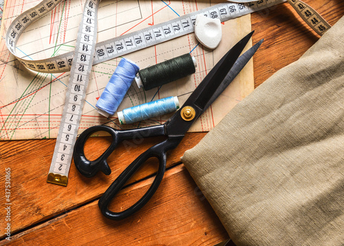 sewing tools, scissors, spools of thread, measuring tape lie on tailors' diagrams and a wooden table