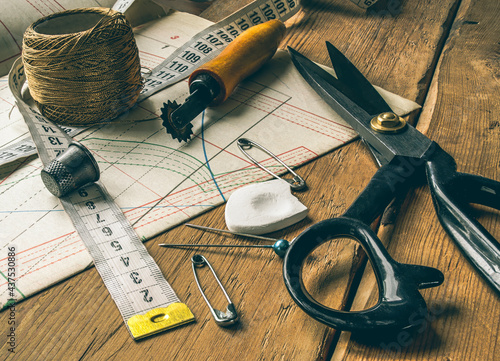 closeup view of retro sewing tools, scissors, chalk, measuring tape lie on tailors' diagrams and wooden table