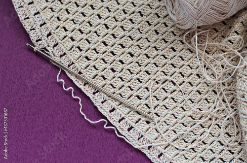 Crocheting with beige cotton threads on a purple background.