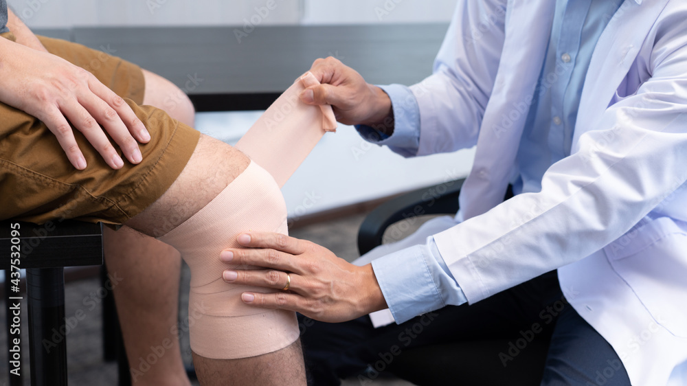 Medical concept a male doctor putting a bandage on knee's male patient after his accident